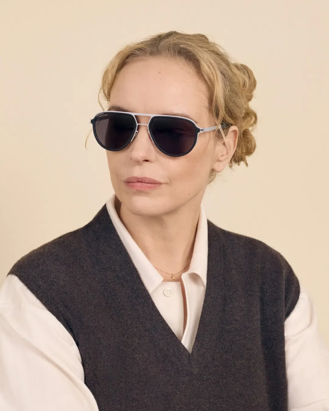 אישה מרכיבה משקפי שמש MYKITA | RIMOWA בסגנון אווייטור עם גשר כפול, על רקע קרם